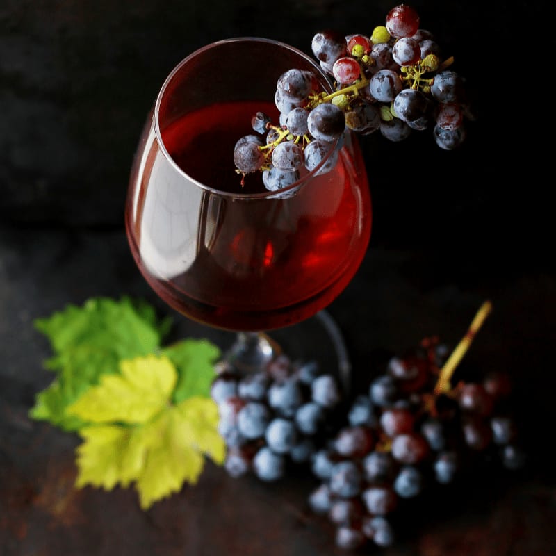 A glass of red wine with grapes and a leaf on a dark surface