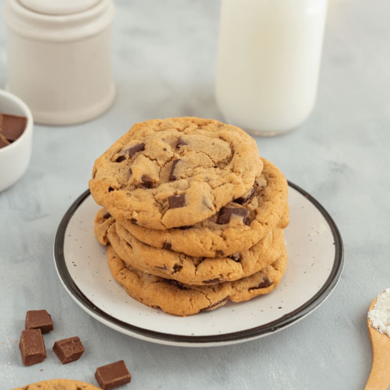 a stack of chocolate chip cookies on a plate next to a glass of milk