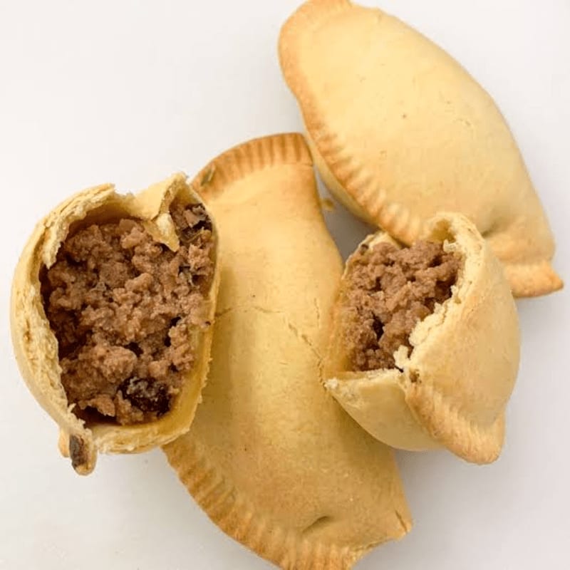 Golden-brown empanadas, some whole and others split open to reveal a savory meat filling, are arranged on a plain white background.