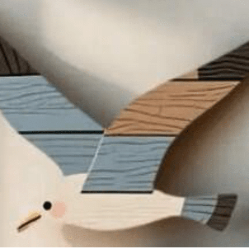 A wooden seagull with colorful wings is displayed against a plain, light-colored wall.