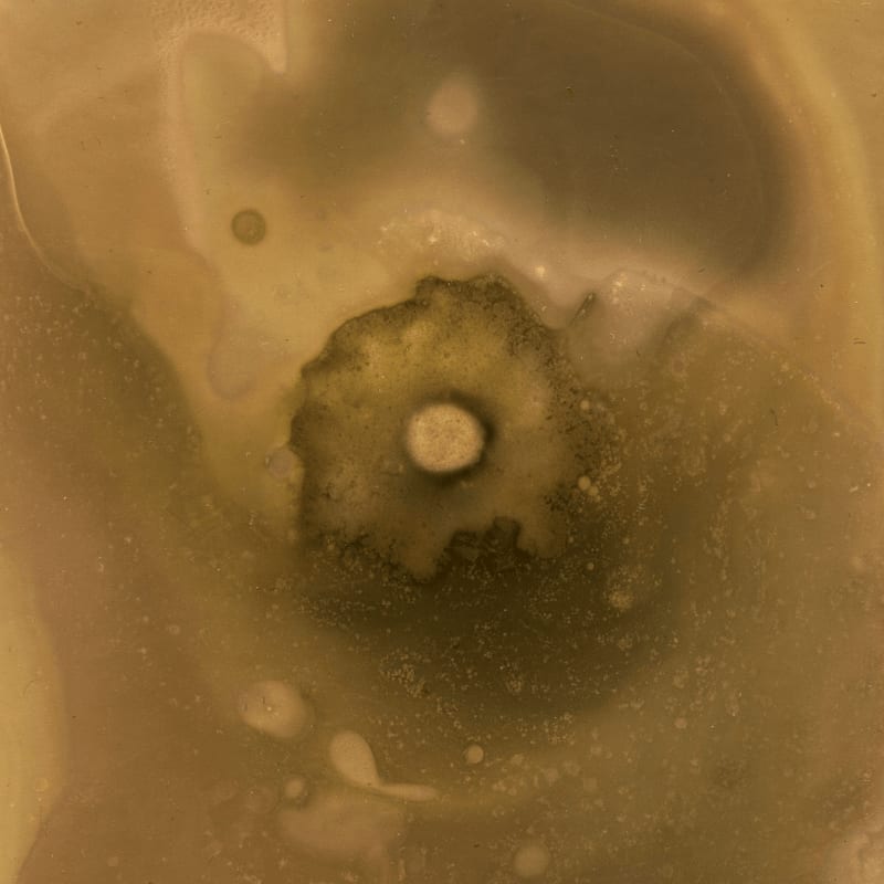A dark, circular impact crater with a bright central peak is surrounded by a diffuse, sandy-colored Martian landscape.
