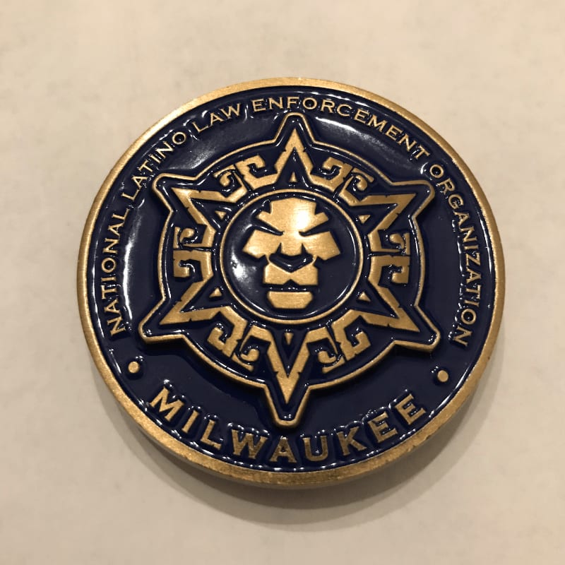 A gold and blue challenge coin with a lion's head emblem is displayed on a light-colored, textured surface.