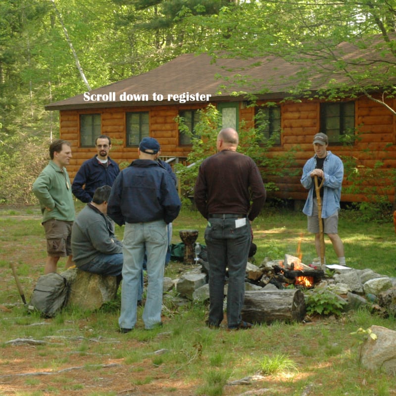 A group of men stand around a campfire in the foreground, with a rustic log cabin and trees in the background.