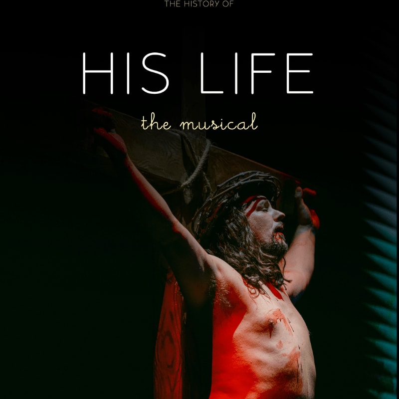 A man portraying Jesus Christ, with a crown of thorns and bloodied torso, is illuminated by red light against a dark, shadowed background with vertical lines.