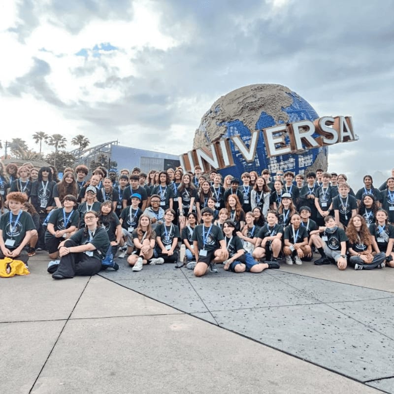 A large group of young people in matching t-shirts poses in front of the iconic Universal Studios globe.