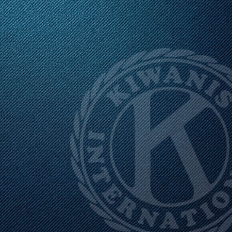 A textured blue background features a faded circular emblem with the letters "KIWANIS INTERNATIONAL" and a large "K" in the center.