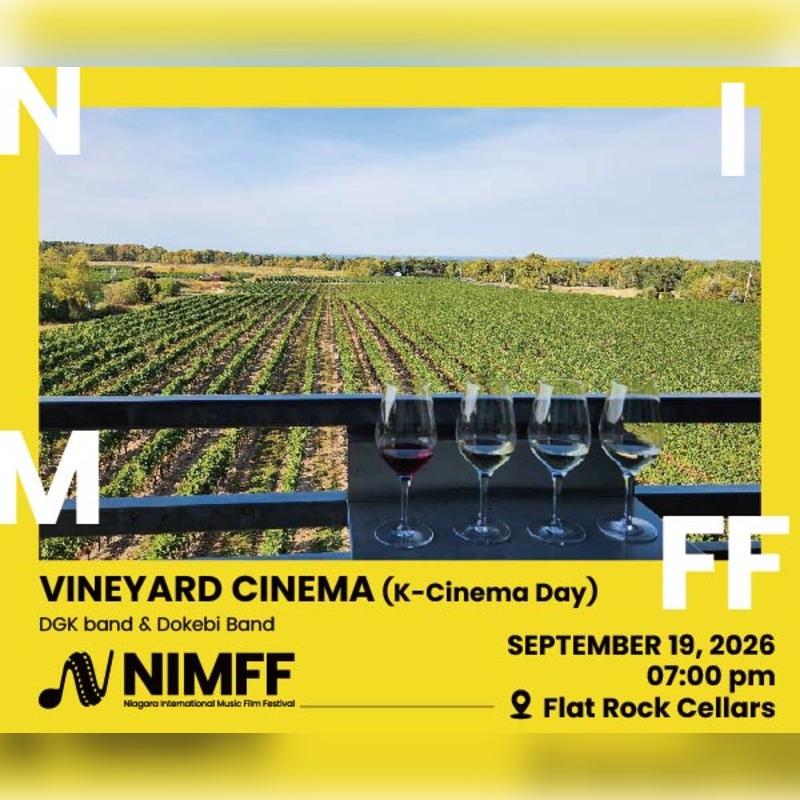Four glasses of wine sit on a railing overlooking a vineyard under a clear sky.