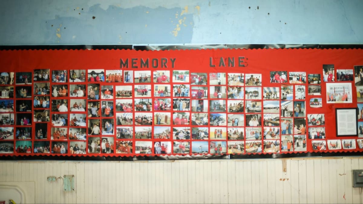 A long bulletin board covered in photographs labeled "MEMORY LANE" hangs on a wall above a tiled surface.