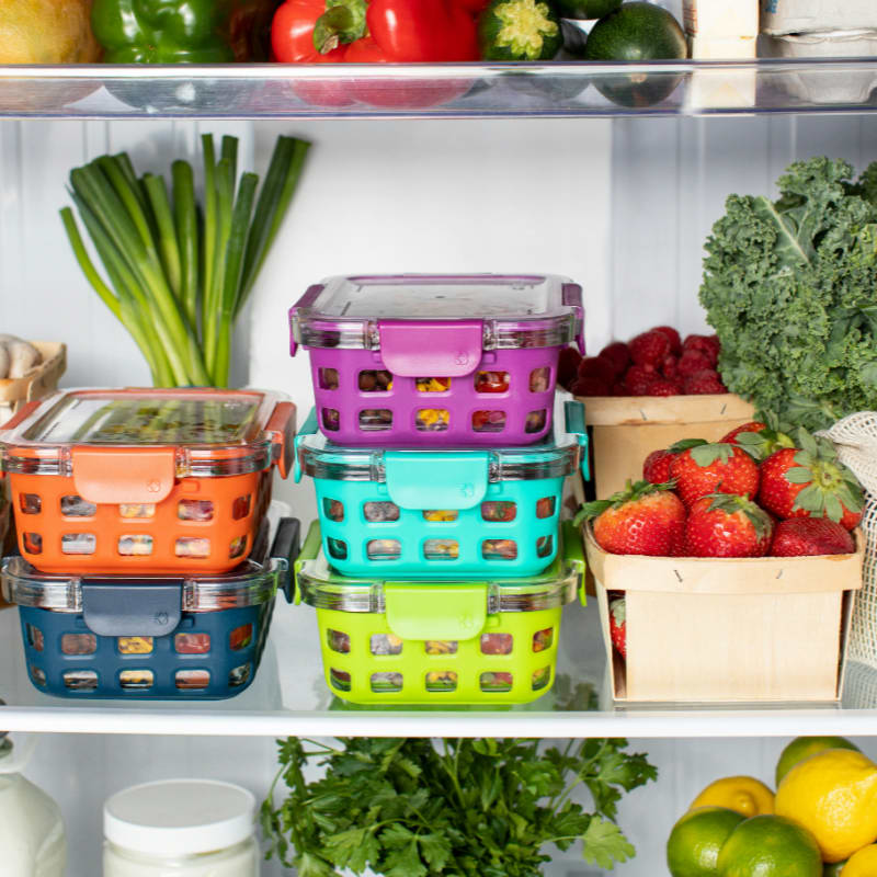 Colorful plastic food containers stacked inside a refrigerator with fresh produce