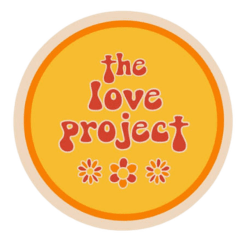 A circular logo with a warm orange background features the words "the love project" in a retro, bubbly font, with three stylized flowers in the foreground.