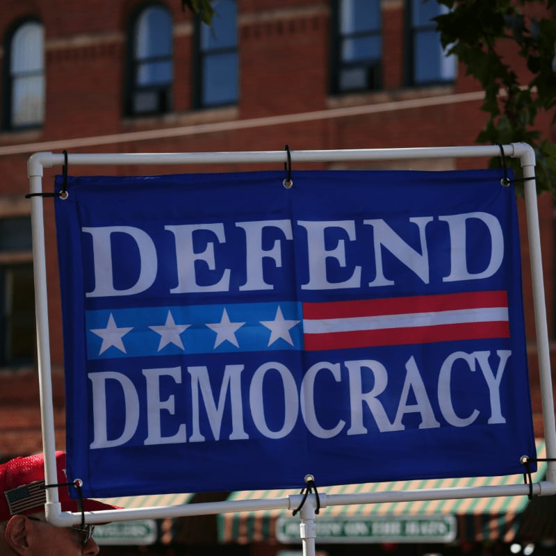 Sign reads "defend democracy" with american flag elements