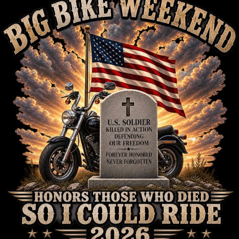 A motorcycle stands beside a tombstone with an American flag waving in the background under a dramatic sky, honoring fallen soldiers.