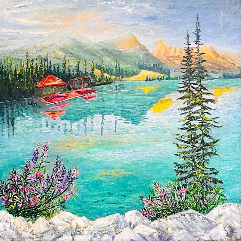 In the foreground, vibrant purple and pink wildflowers bloom beside white rocks, while the background features a serene turquoise lake reflecting a red boathouse and distant, sun-kissed mountains.