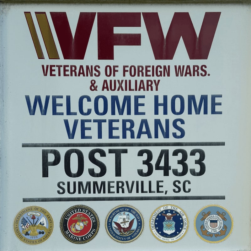 A sign for VFW Post 3433 in Summerville, SC, with the VFW logo and military seals in the foreground, is set against a plain background.