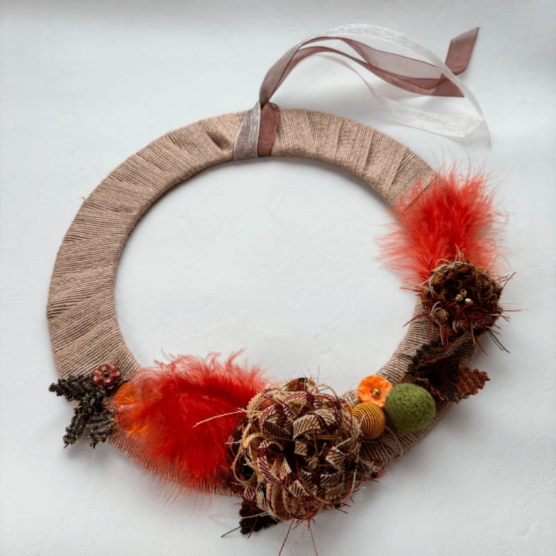 A rustic wreath adorned with feathers and natural elements hangs against a plain white background.