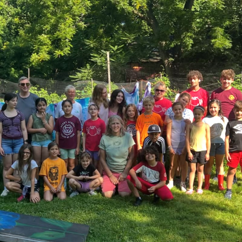 A group of children and adults pose for a photo in a grassy yard with trees in the background.