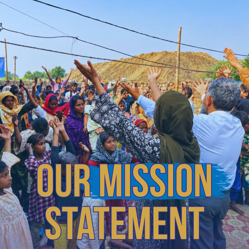A diverse group of people with their hands raised in worship are gathered in the foreground, with a large pile of hay and a clear blue sky in the background.