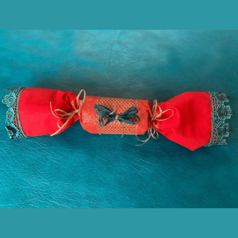 A festive red Christmas cracker with teal lace trim lies on a textured teal background.