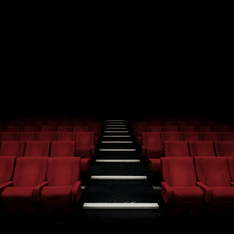 Rows of empty red theater seats recede into a dark background with illuminated steps leading upwards.