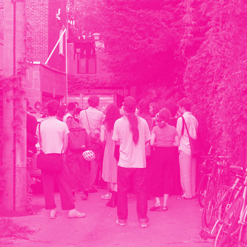 A group of people stand in a courtyard with bicycles parked to the right, all bathed in a vibrant pink hue.