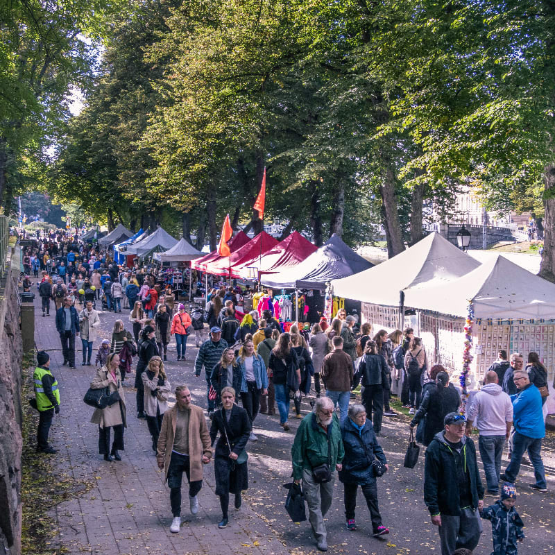 a crowd of people walking around a park with tents