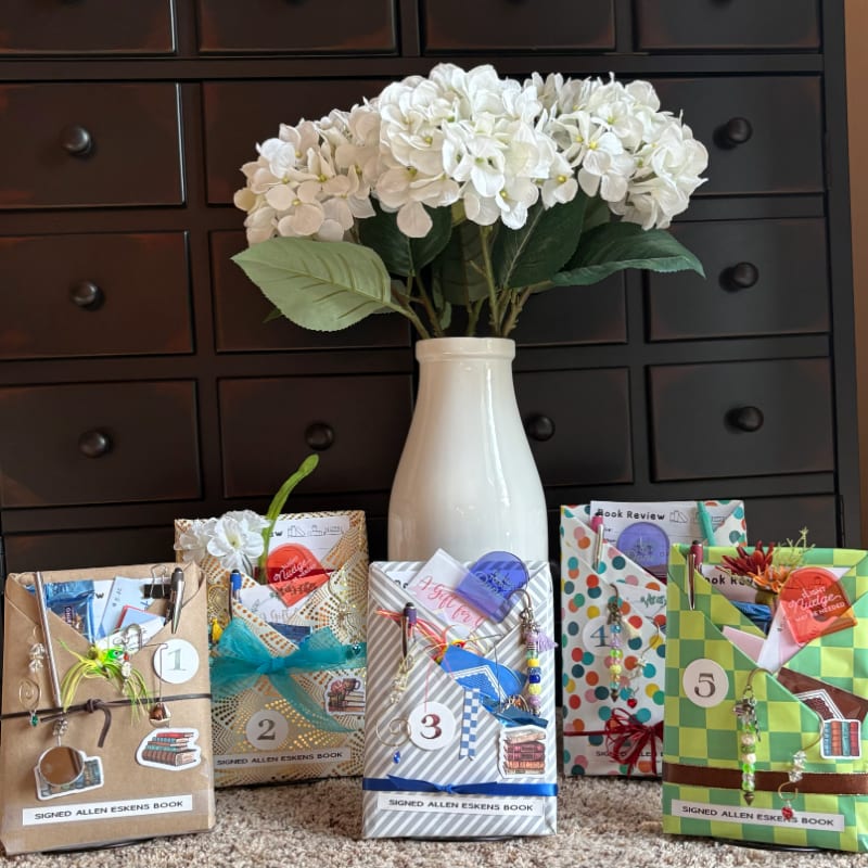Five wrapped books with numbered tags and decorative elements sit on a textured surface in front of a white vase filled with white hydrangeas, all set against a dark wooden dresser.