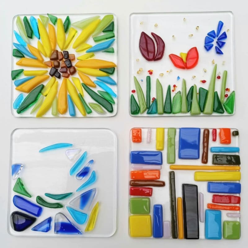 Four square glass art pieces, each with a unique design of colorful glass shards, are arranged on a white background.