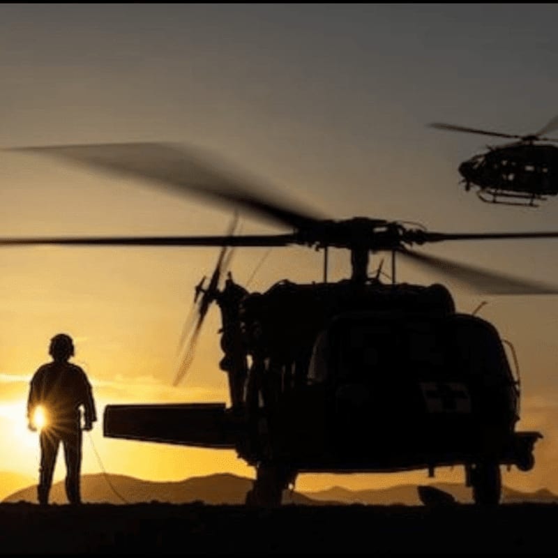 A soldier stands silhouetted against the sunset in the foreground, with helicopters in the midground and background.