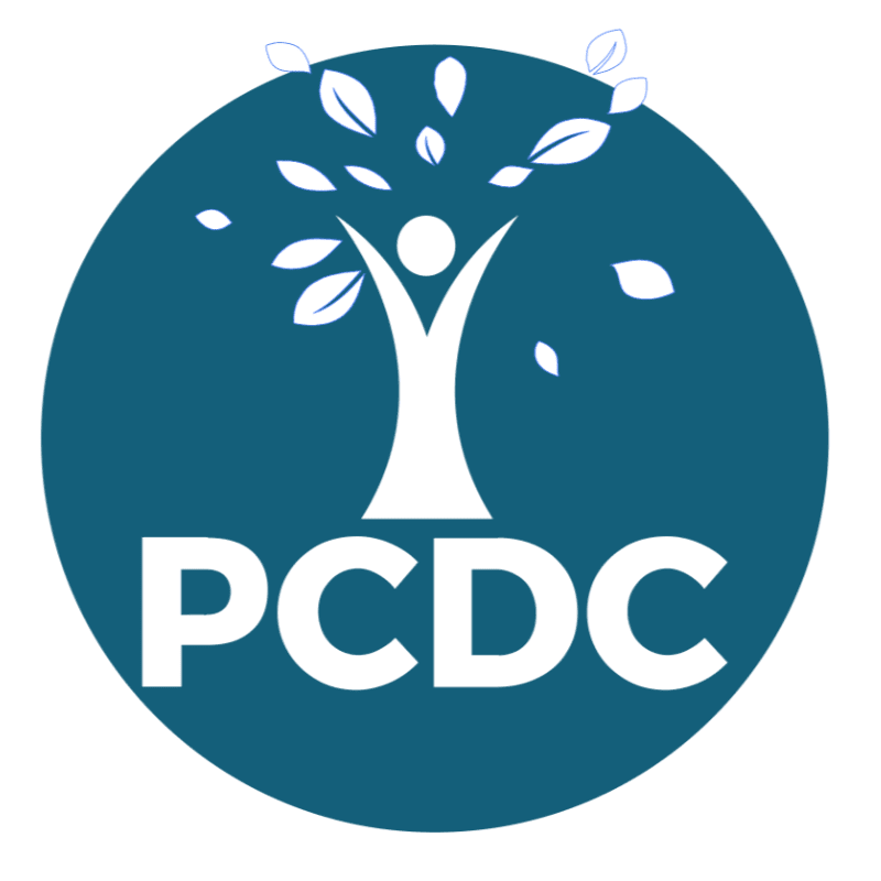 A white stylized tree with a human-like figure at its base and leaves at the top stands within a teal circle, with the letters "PCDC" in white below the figure.
