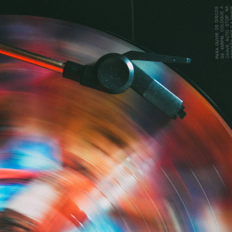 A spinning, colorful vinyl record with a stylus in the foreground is set against a dark, blurred background.