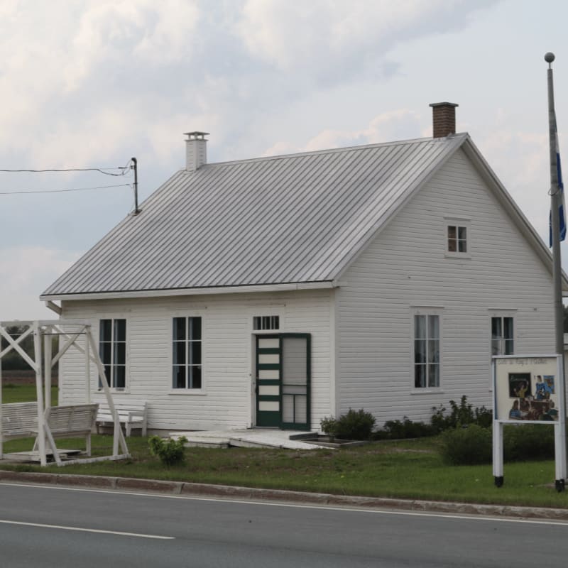 A white clapboard house with a green door and a swing set in the foreground stands against a cloudy sky.