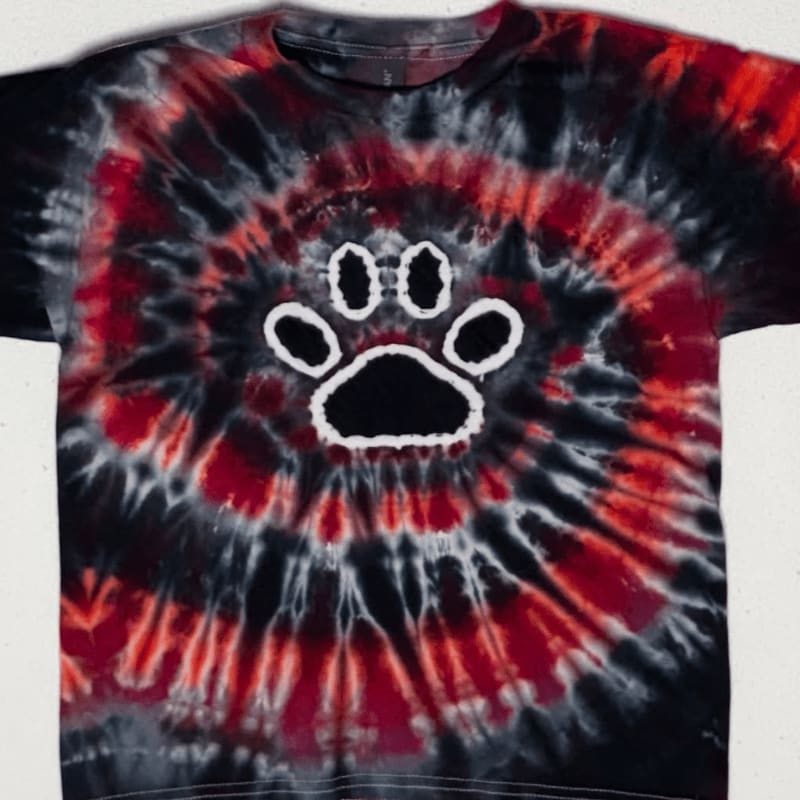 A black and red tie-dye t-shirt with a white paw print design is displayed against a plain background.