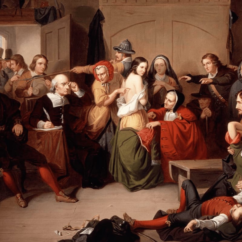 In the foreground, a man in red pants lies on the floor amidst scattered papers, while in the background, a woman is being examined by a group of people in a dimly lit room.