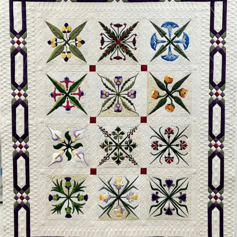 A cream-colored quilt with a grid of twelve intricate floral blocks is bordered by a geometric pattern of purple and burgundy.