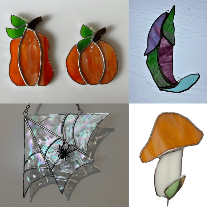 Four stained glass ornaments, two pumpkins in the top left, a leaf in the top right, a spiderweb with a spider in the bottom left, and a mushroom in the bottom right, are displayed against a plain background.