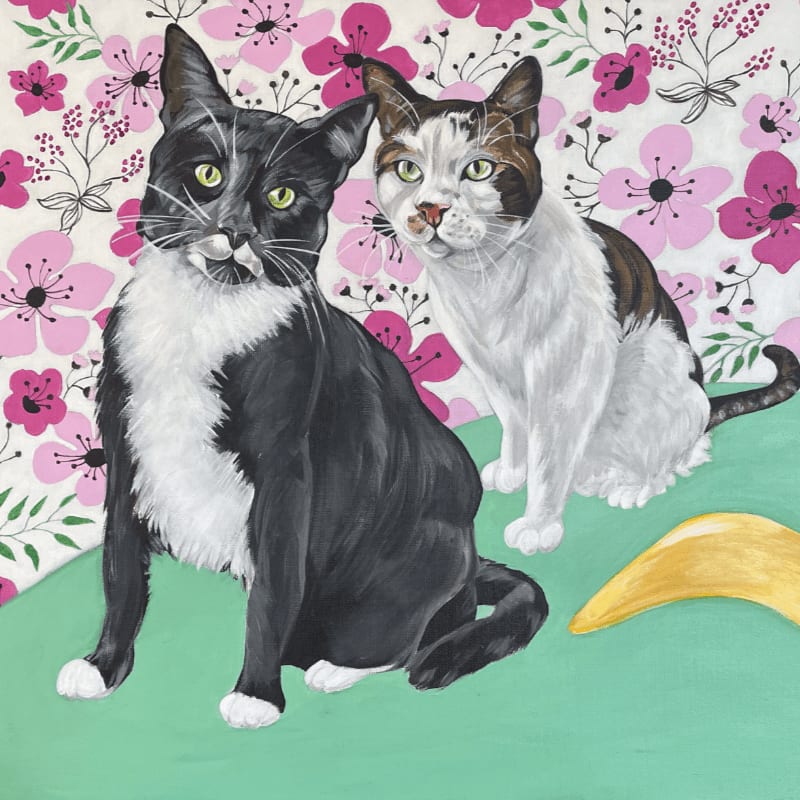 Two cats, one black and white and the other white with brown markings, sit on a mint green surface in front of a floral patterned background.