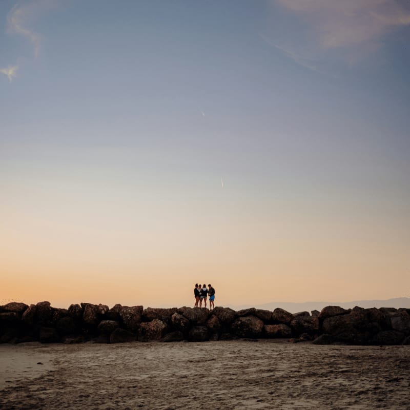 silhouette of people standing on rock formation near body of water during sunset