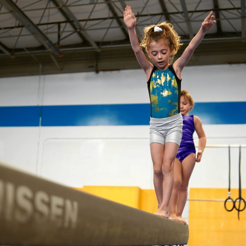 a person jumping on a trampoline with a child in the background