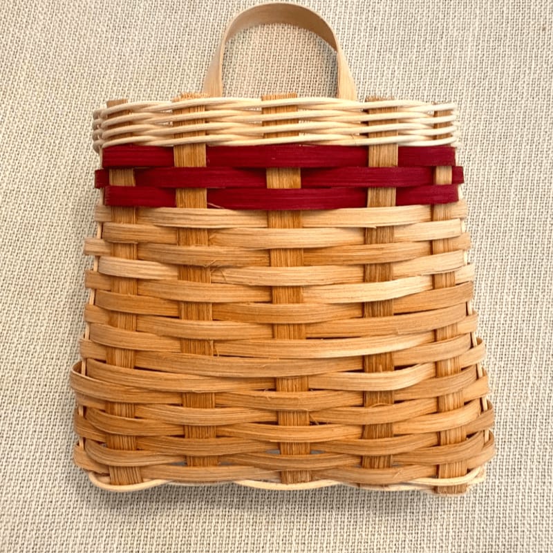 A woven basket with a red stripe and a wooden handle sits on a textured, light-colored surface.