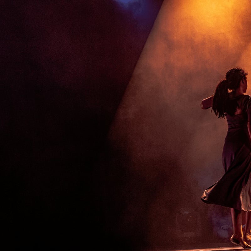 A woman in a dark dress dancing on stage under warm orange light