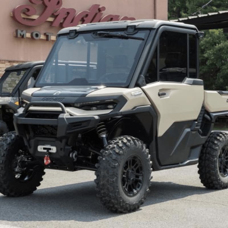 A tan utility vehicle with large tires sits in the foreground, with a building featuring an "Indian Motorcycle" sign in the background.