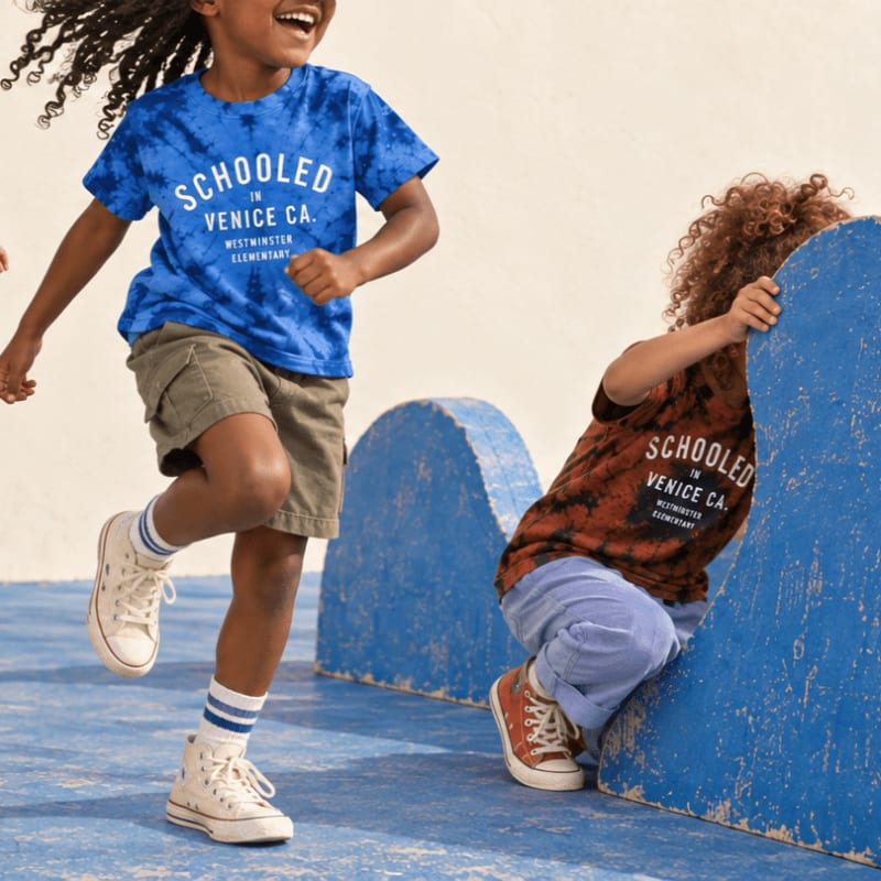 Two children in tie-dye shirts play near a blue structure against a light-colored background.