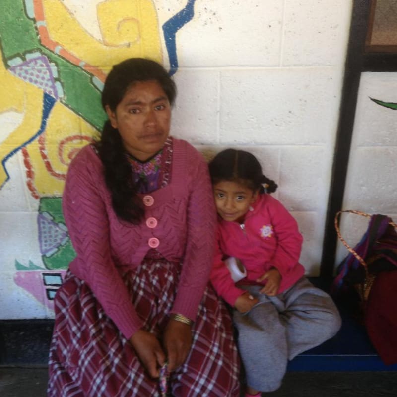 A woman and a young girl sit in front of a colorful mural.