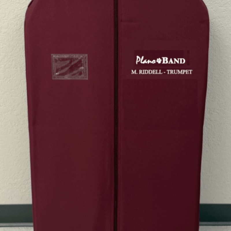 A maroon garment bag with a clear window and "Plano Band M. Riddell - Trumpet" printed on it stands against a plain wall.