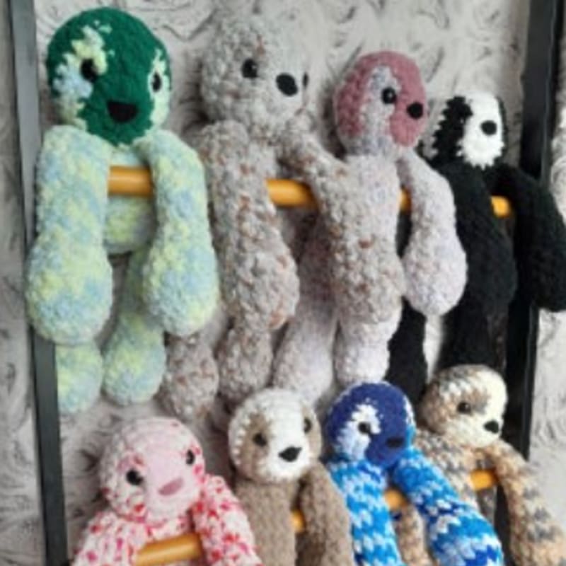 A row of colorful, crocheted stuffed animals with long limbs hang from yellow bars in the foreground, against a textured, light-colored background.