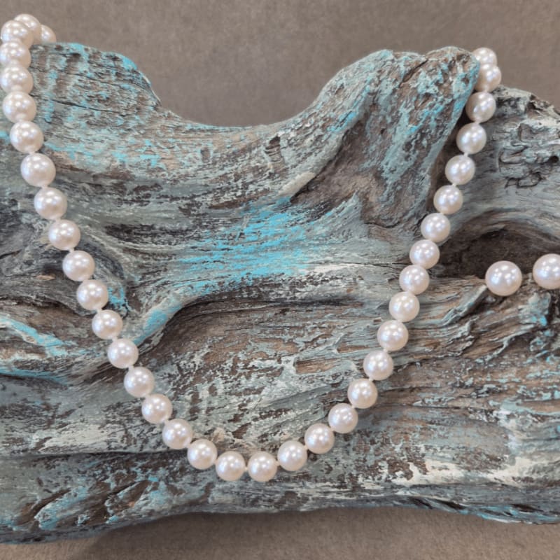 A pearl necklace rests on a weathered, turquoise-painted piece of driftwood, set against a plain gray background.
