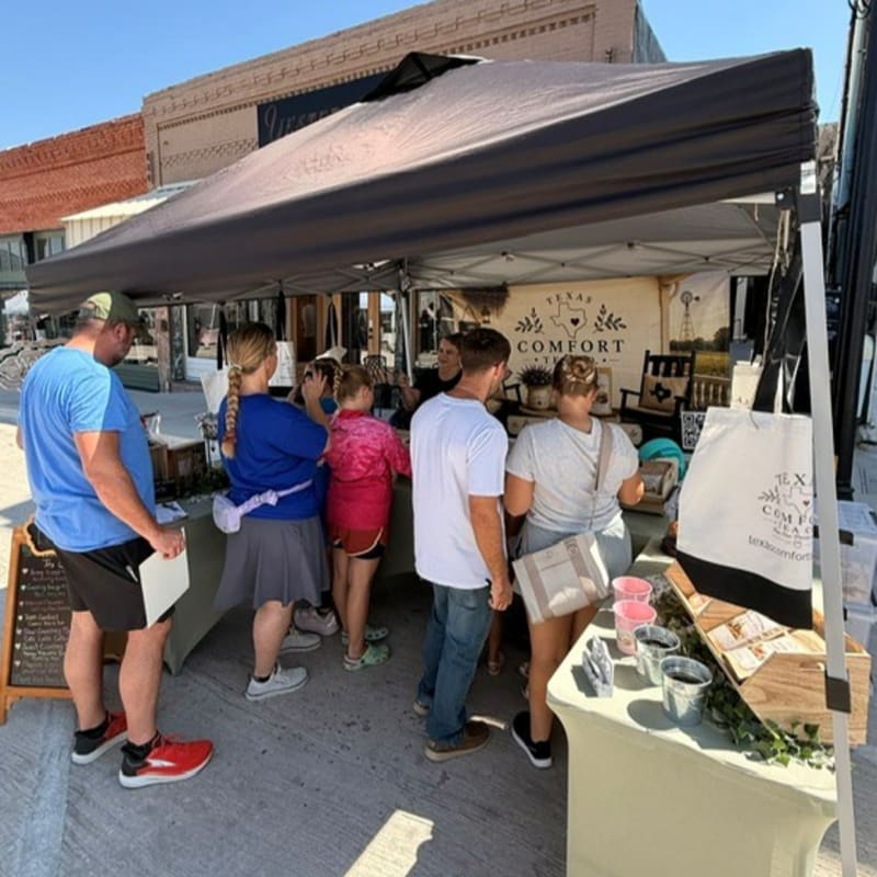 People browse items at an outdoor market stall with a brick building in the background.