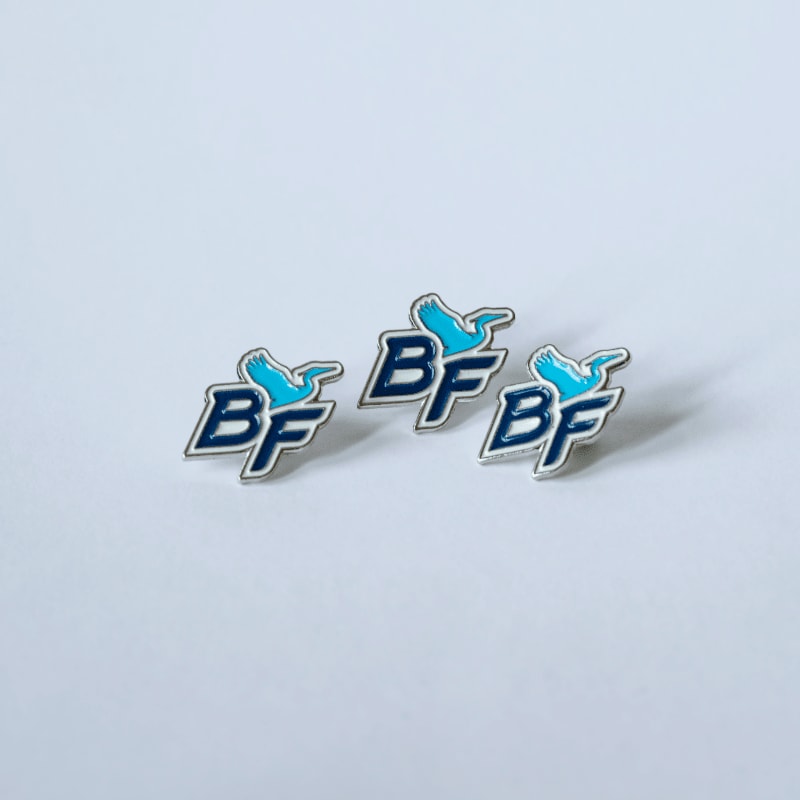 Three blue and silver enamel pins with a bird and "BF" logo are arranged on a plain white background.