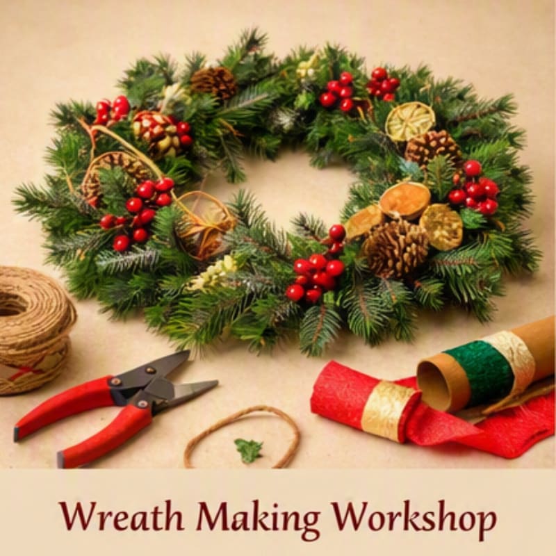 A festive evergreen wreath decorated with red berries and pinecones sits behind a pair of red-handled shears and crafting supplies on a neutral background.