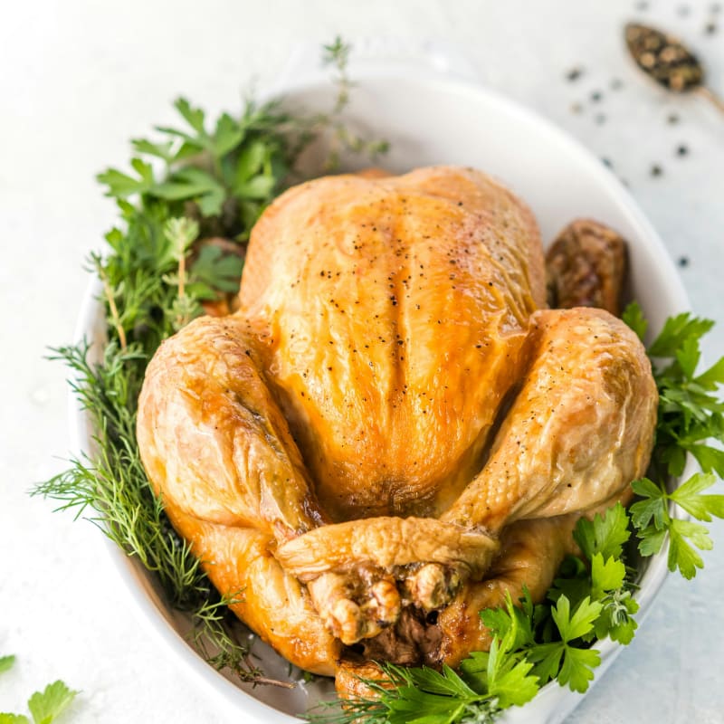a roasted turkey in a white bowl with fresh herbs
